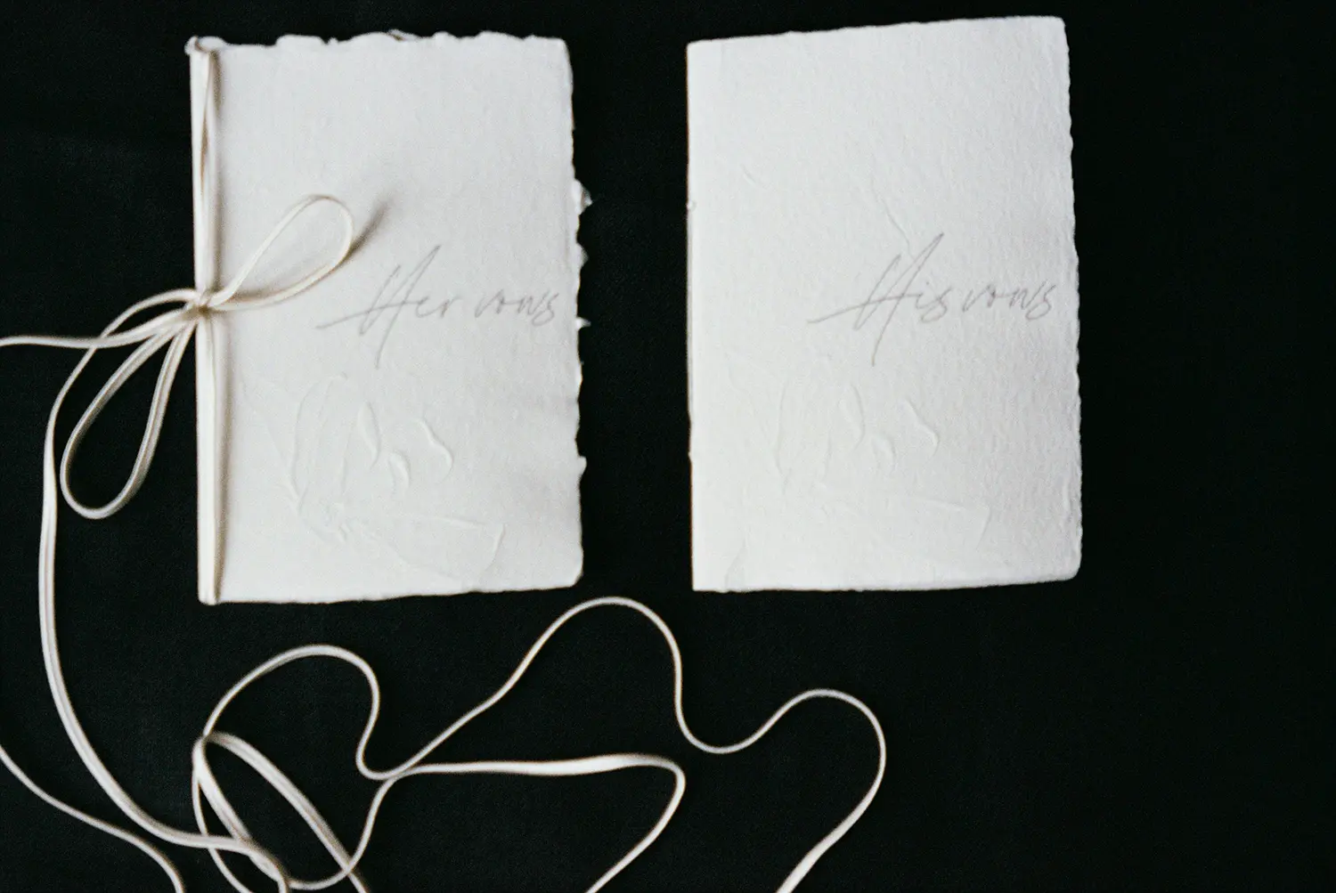 Handwritten wedding vows in white, natural paper covers, tied with a simple string, elegantly placed on a black backdrop.