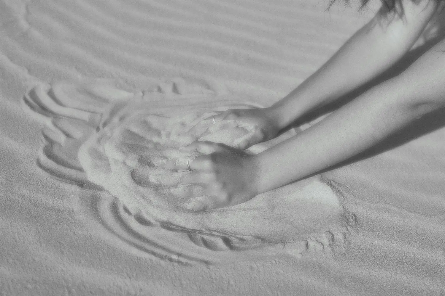 A close-up of two hands drawing a heart in the sand on a beach, symbolizing love and connection.